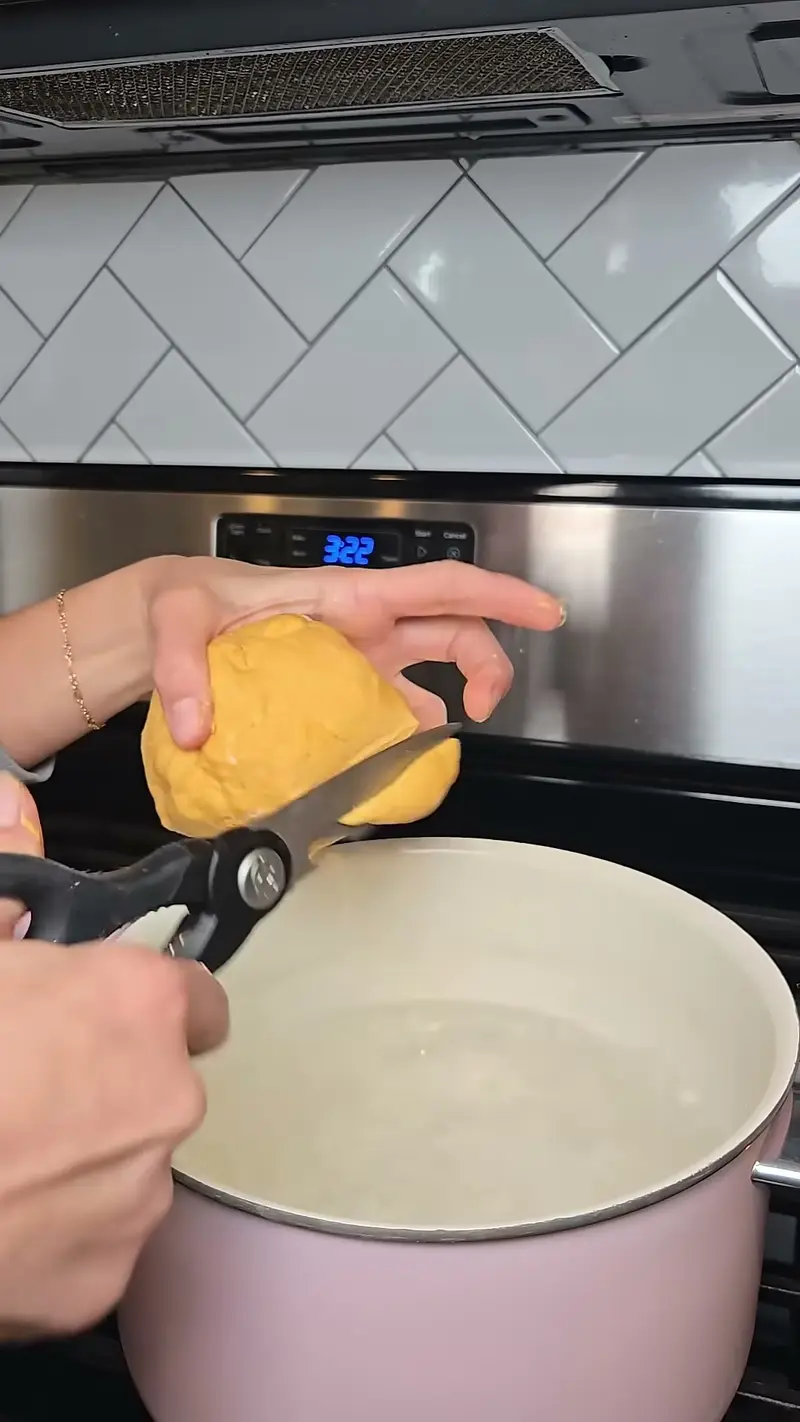 Crystal snipping pumpkin gnocchi dough into pieces with kitchen scissors over a pot of boiling water