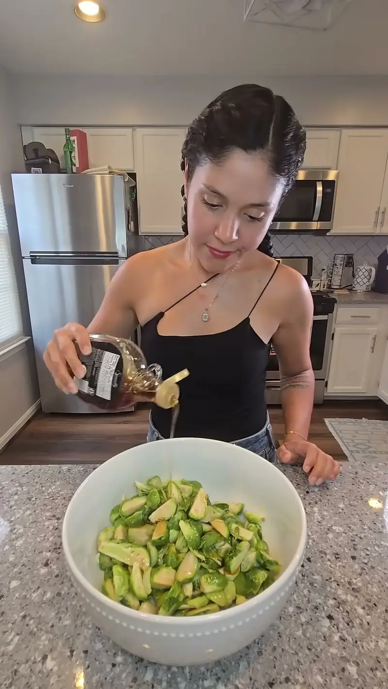 Crystal drizzling oil over a white bowl of halved brussels sprouts