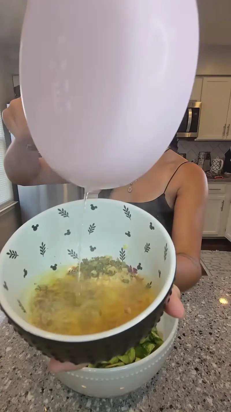 Pouring the bang bang sauce from a pink measuring cup into the bowl of sprouts