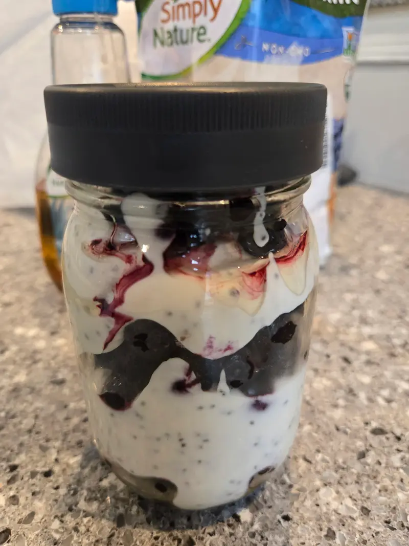 A jar of blueberry cheesecake chia pudding layered with white yogurt and dark blueberry compote