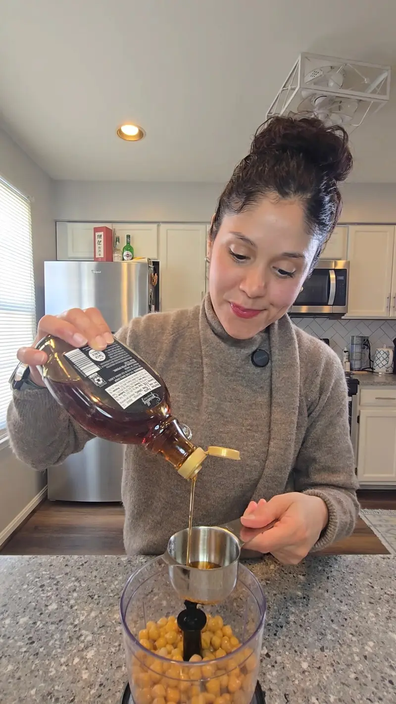 Crystal pouring maple syrup into a food processor full of chickpeas