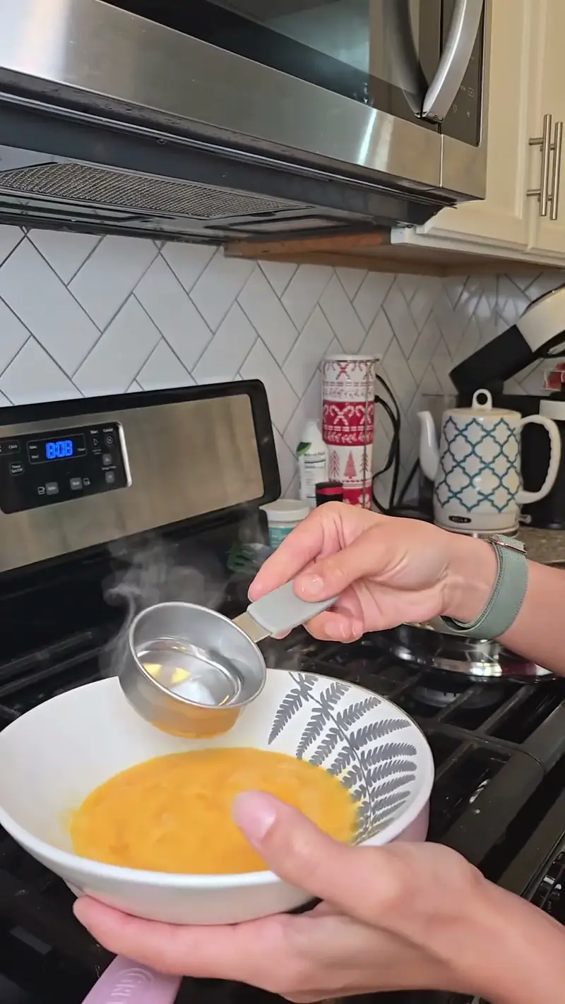 Crystal pouring water from a measuring cup into the beaten egg
