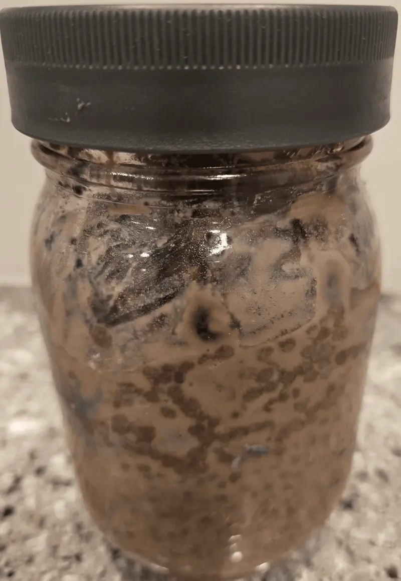 A jar of chocolate protein chia pudding with chocolate chips through it