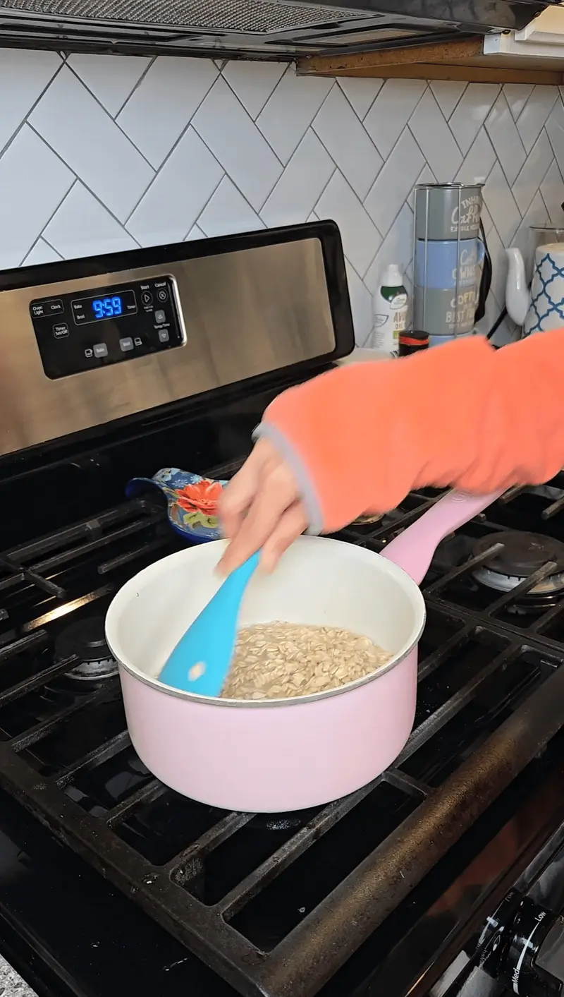 Stirring the oats in the pink saucepan with a blue spatula
