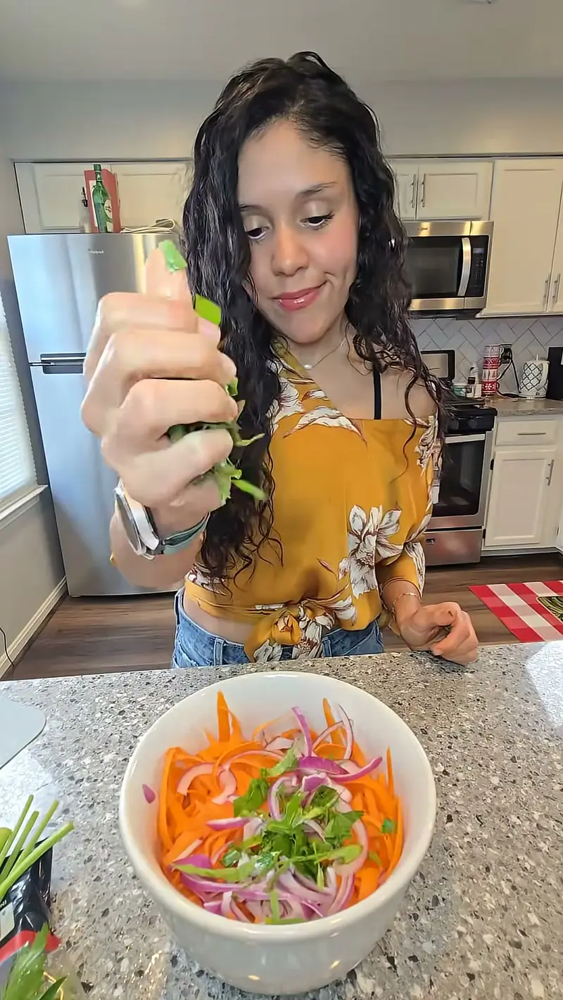 Crystal holding up a sliced spring onion above a bowl of shredded carrot and red onion