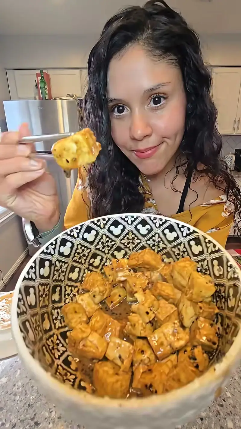 Crystal in her kitchen holding a forkful of crispy tofu
