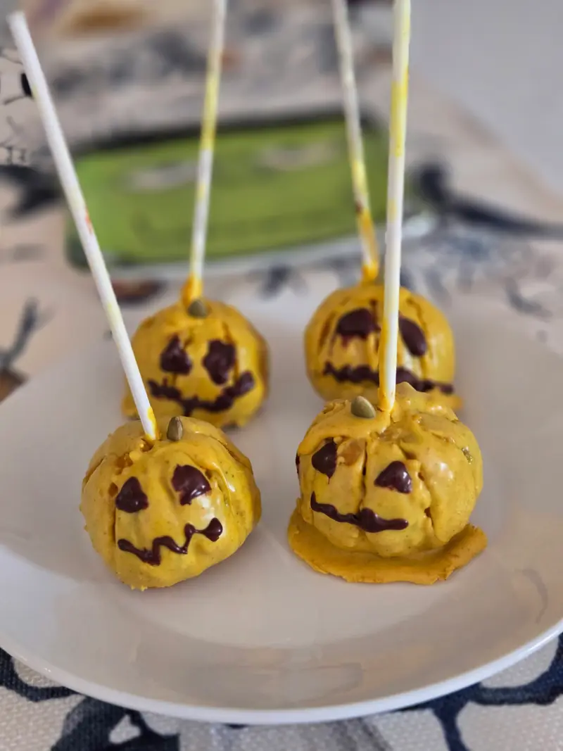 Four pumpkin-shaped cake pops with jack-o'-lantern faces on a plate