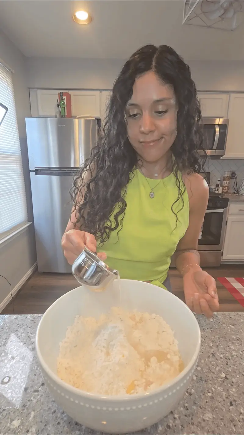 Crystal adding water to the empanada dough in a large white bowl