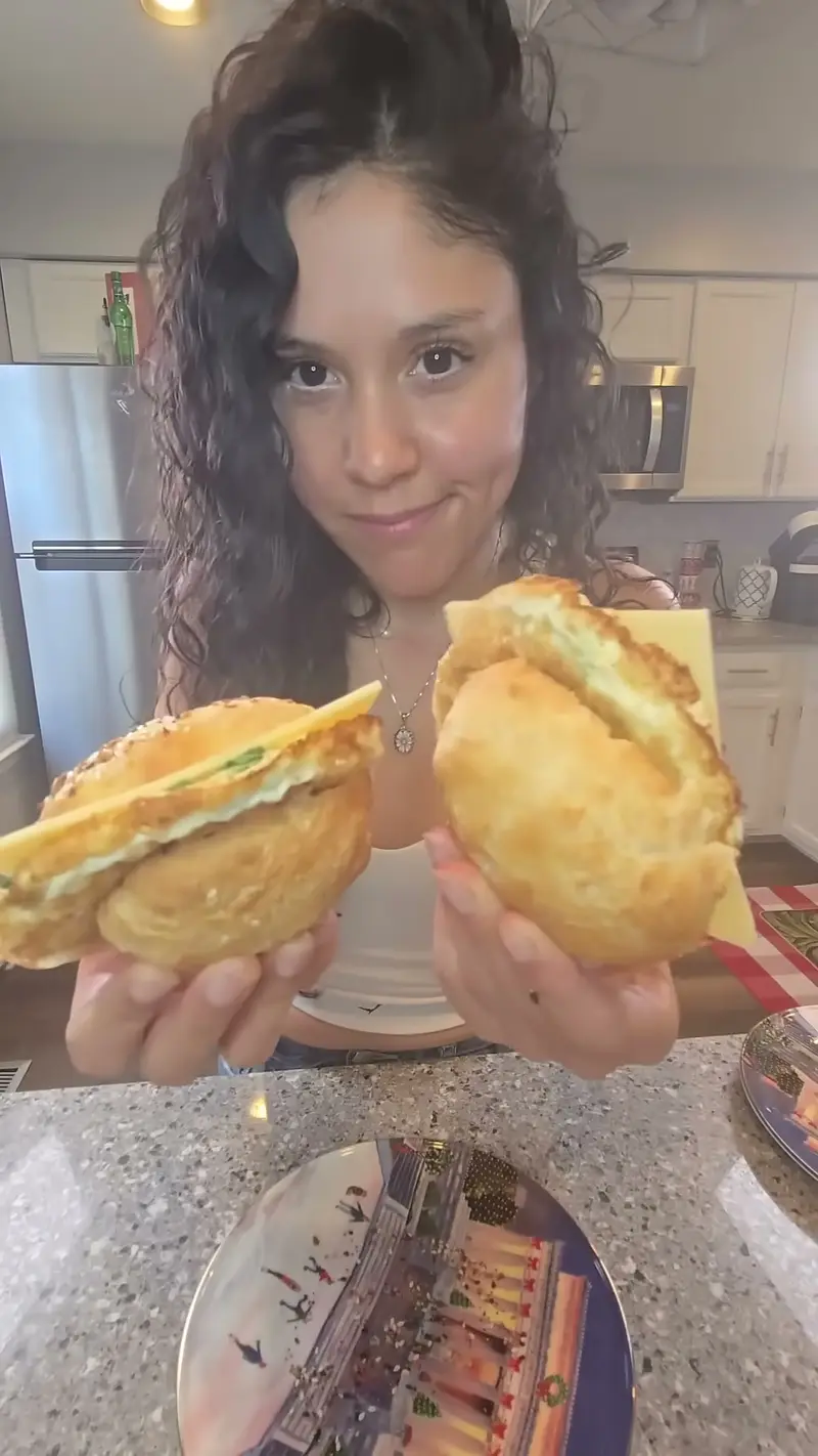 Crystal holding up two halves of a Greek yogurt bagel breakfast sandwich