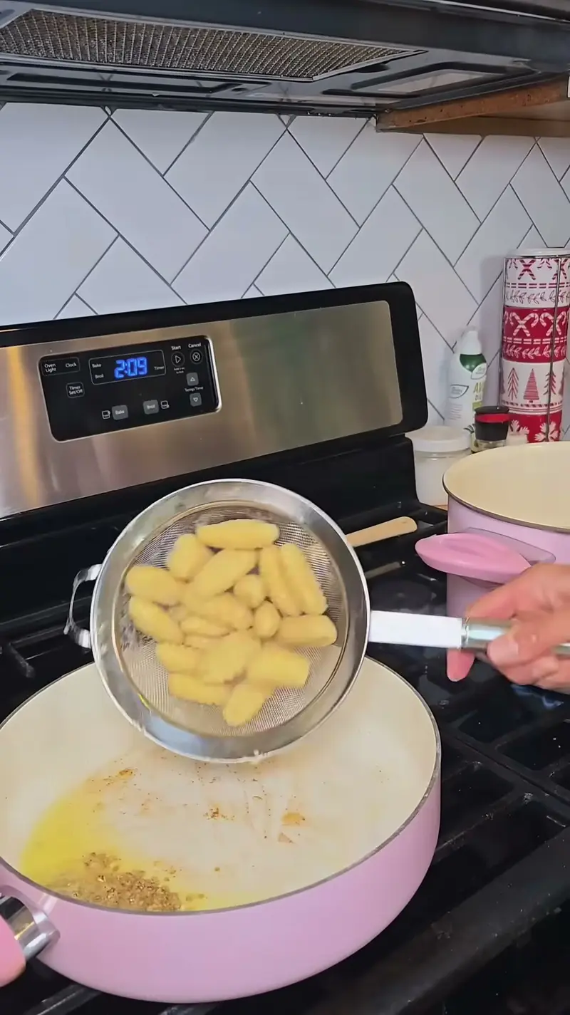 Crystal tipping cooked pasta from a strainer into a pink pan