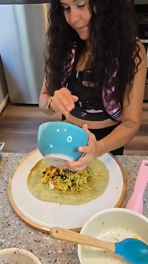 Crystal tipping the scrambled filling from a blue bowl onto a spinach tortilla