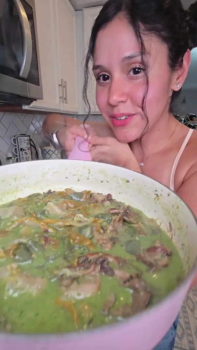 Crystal leaning over a pink pot of creamy pesto mushroom pasta