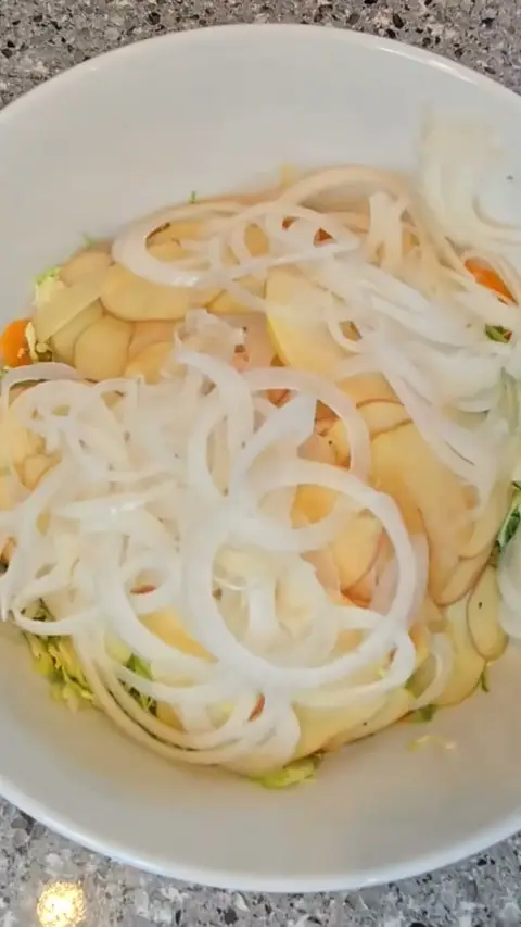 Sliced onion and apple layered over shredded brussels sprouts in a white bowl