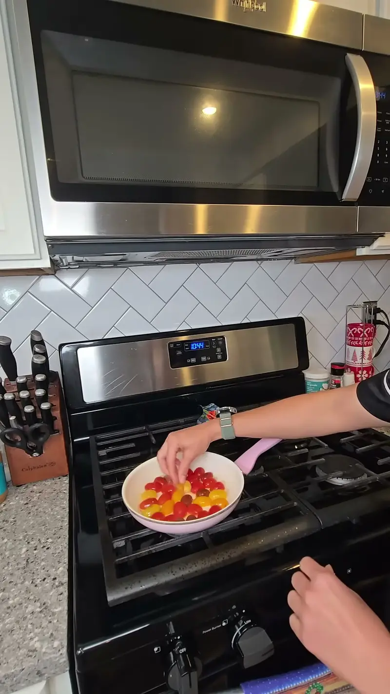 Crystal setting a pink pan of halved cherry tomatoes on the stove