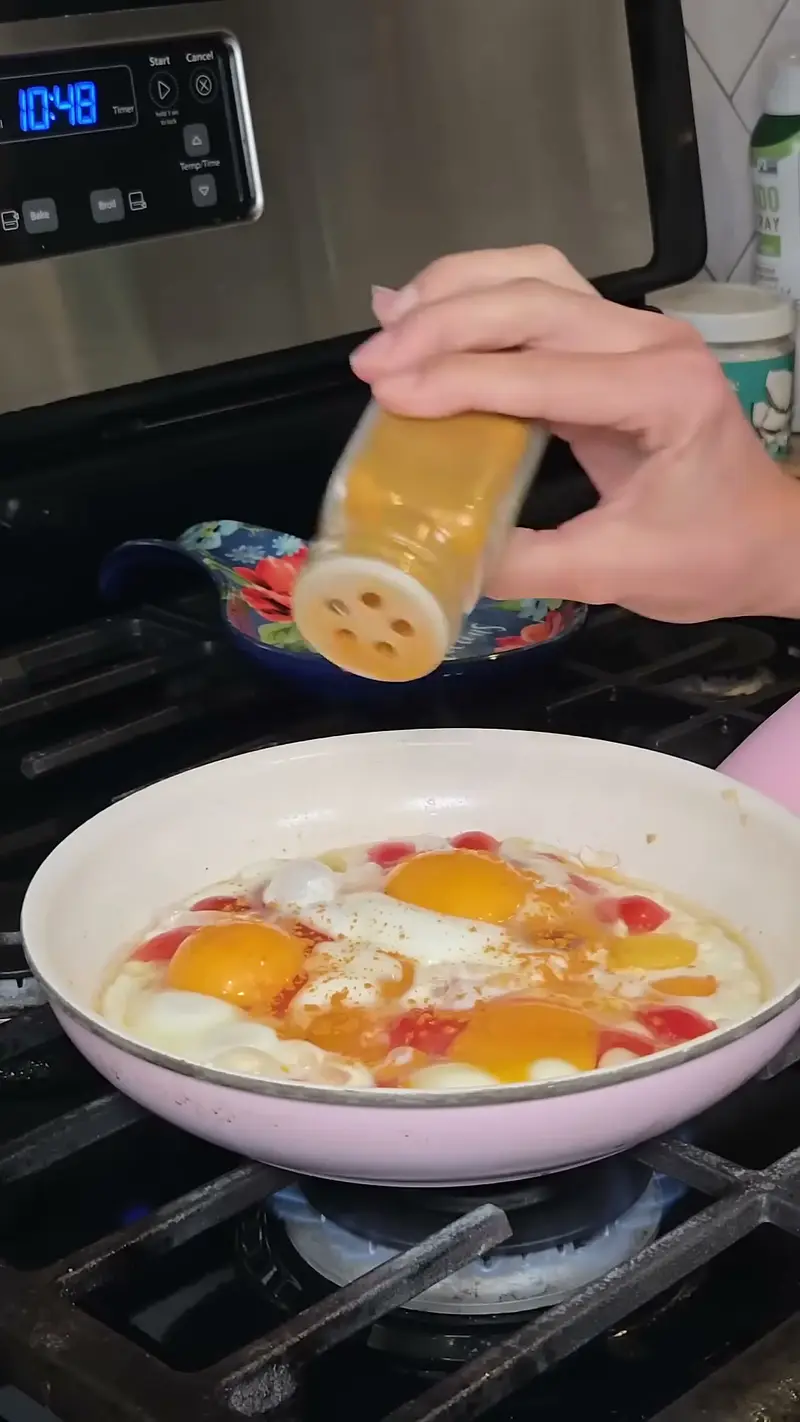 Crystal shaking seasoning over eggs cooking among the tomatoes
