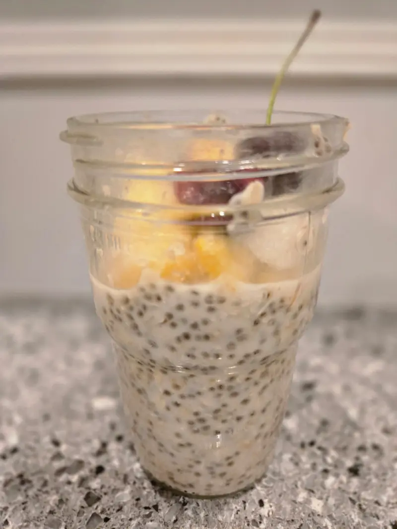 A glass of chia pudding topped with pineapple chunks and a cherry