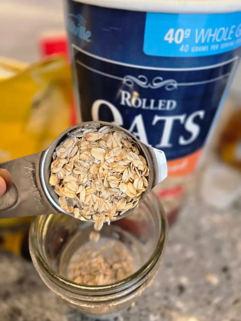 Tipping a measuring cup of rolled oats into a mason jar