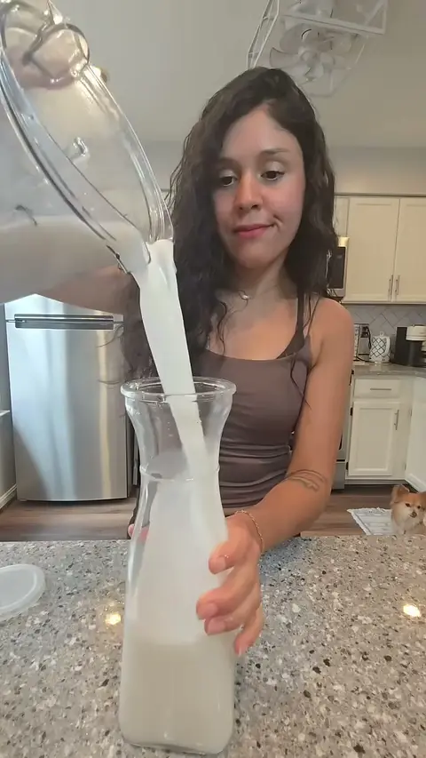 Crystal pouring fresh plant milk from the blender jug into a glass carafe