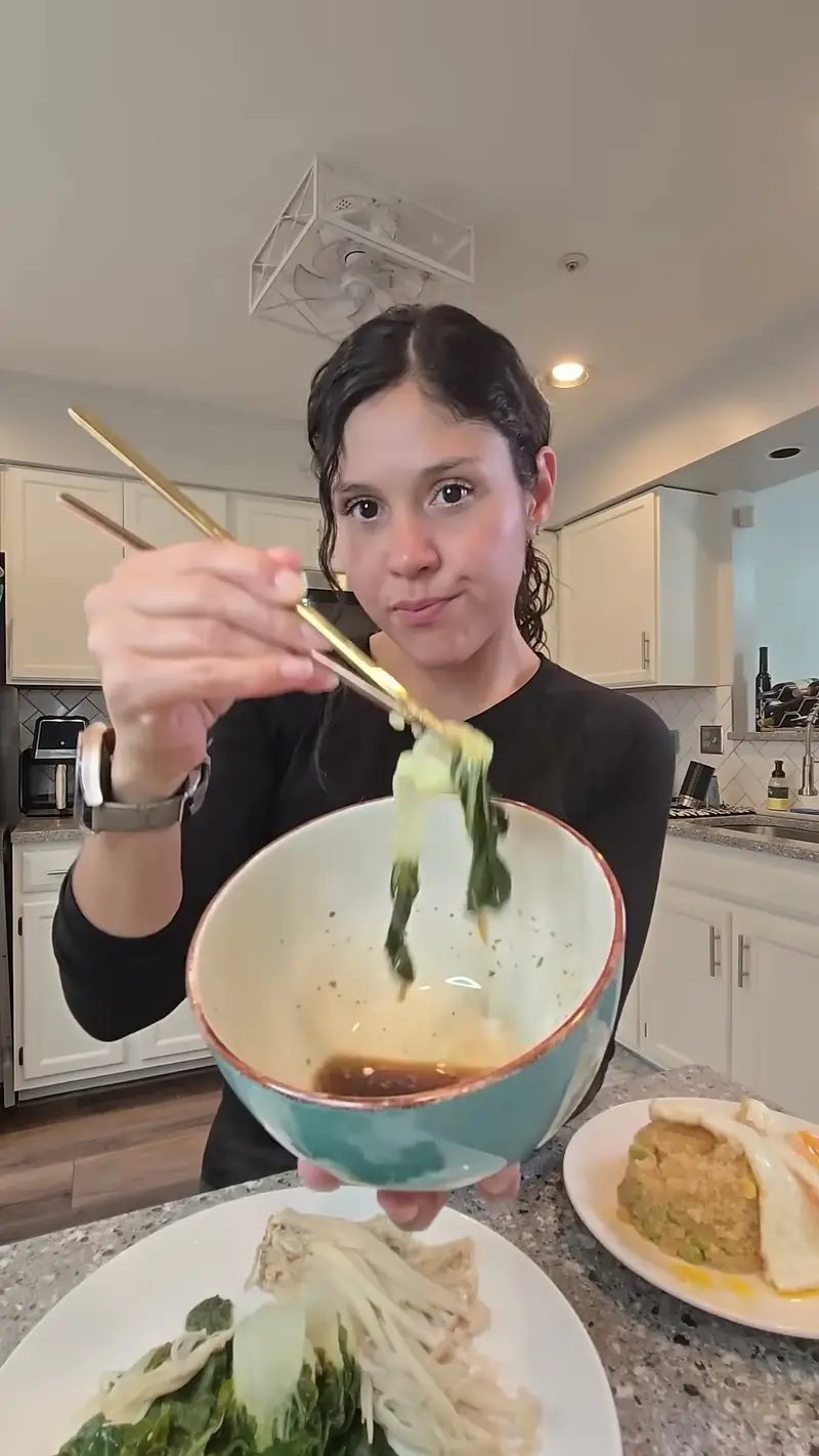 Crystal lifting steamed greens with chopsticks over a quinoa bowl