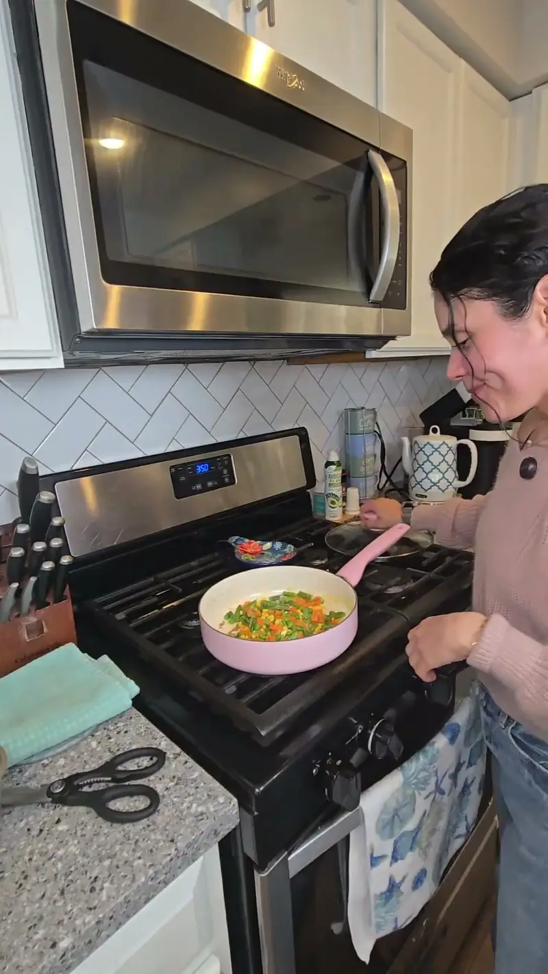 Crystal cooking diced vegetables in a pink pan on the stove