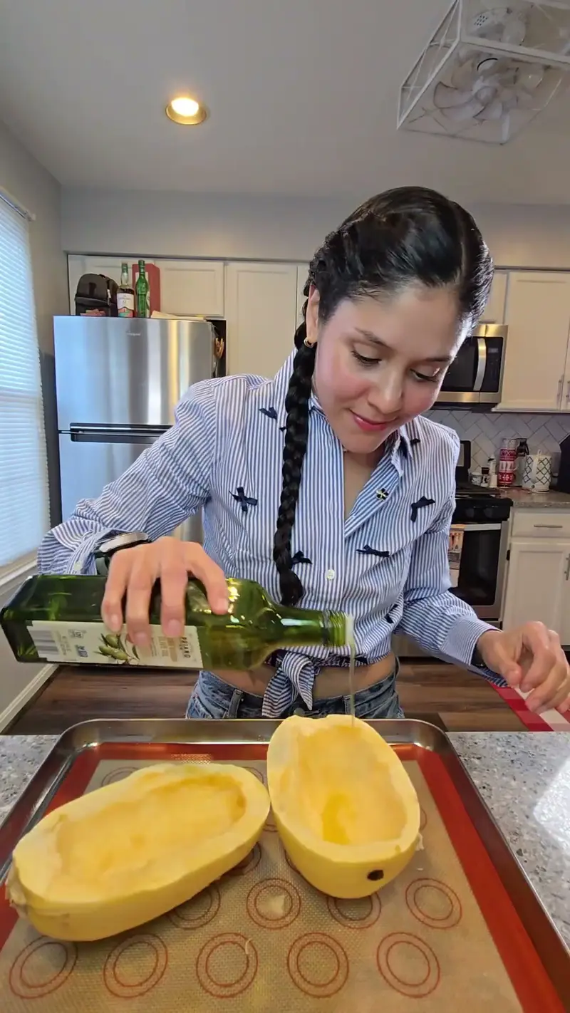 Crystal drizzling olive oil over two halves of spaghetti squash on a baking tray