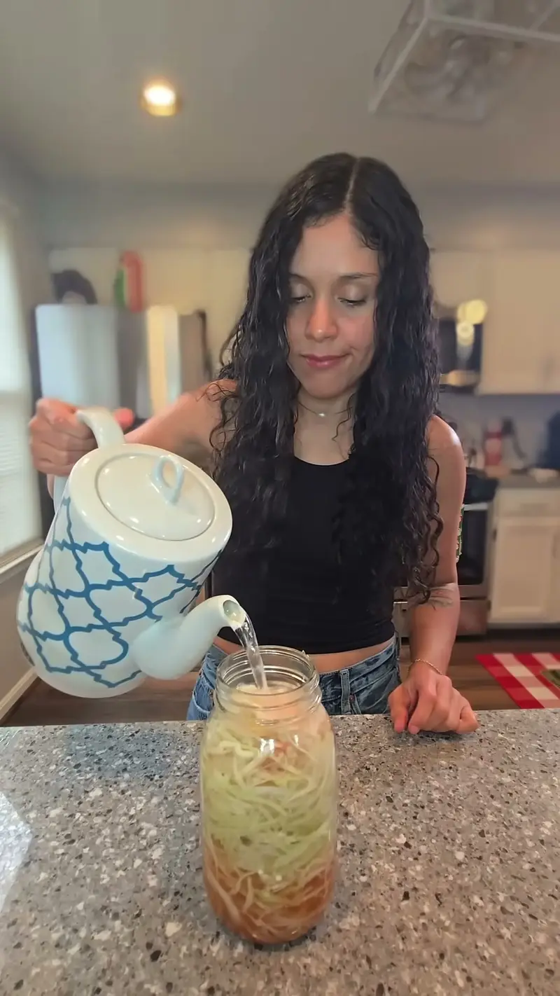 Crystal pouring hot water from a kettle into a jar of cabbage noodles