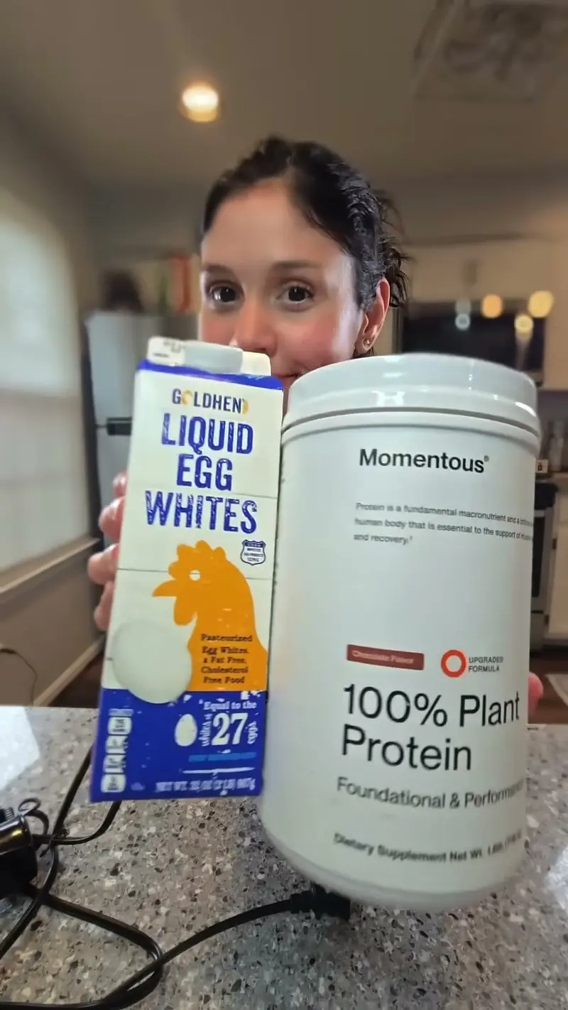 Crystal holding up the carton of liquid egg whites and the tub of chocolate plant protein